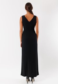 Abito maxi nero senza maniche con scollo a V sul retro, con una vestibilità su misura, pieghe in vita e una texture liscia, abbinato a tacchi alti neri.