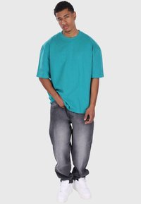 Turkusowy, oversized t-shirt, krótki rękaw, w połączeniu z jasnoszarymi, postarzanymi dżinsami i białymi trampkami. Prosty design, luźny krój.