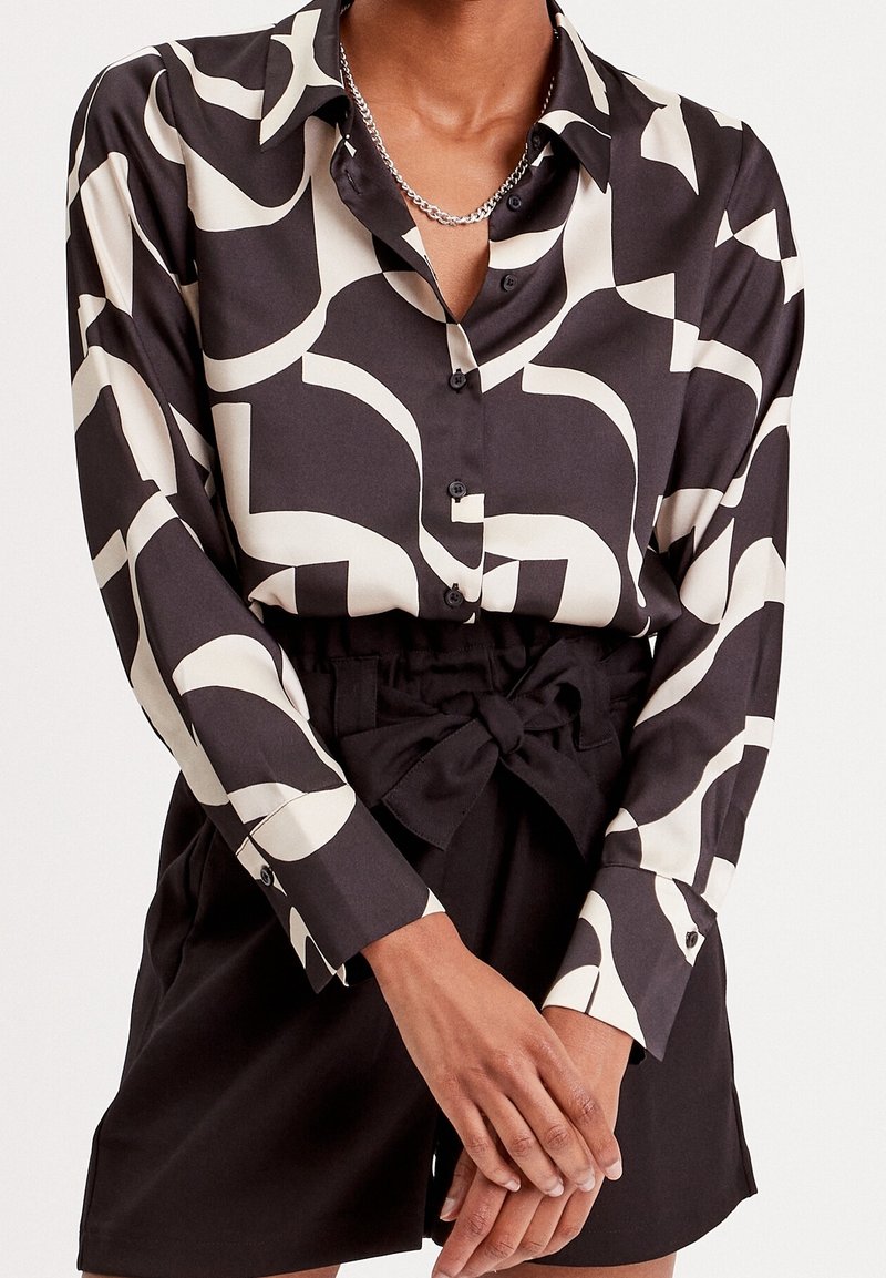 Langsleeve knoopshirt in het zwart met een crème abstract patroon, gemaakt van gladde stof, gecombineerd met zwarte high-waisted shorts met een strik.