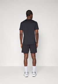 Black short-sleeve athletic shirt with a round neckline, paired with black shorts. Features smooth texture and athletic fit, worn with white socks and sneakers.