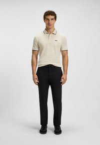 Polo shirt crema con dettagli neri, abbinato a pantaloni neri e scarpe nere. Design minimalista, vestibilità dritta e colletto classico.