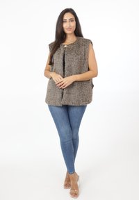 Faux fur-väst i grått, ärmlös design med rund halsringning, framknäppning och mjuk textur, tillsammans med blå skinny jeans och klara klackar.