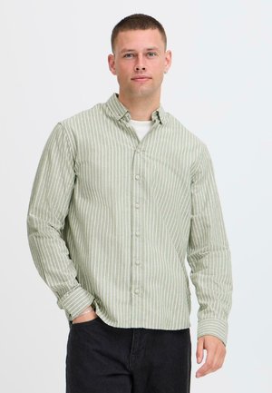 Grün-weiß gestreiftes Hemd mit Knöpfen, Kragen, langen Ärmeln und Knopfleiste vorne, gefertigt aus einem strukturierten Stoff. Kombiniert mit dunkler Hose.