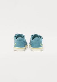 Modré plátěné boty s texturovaným povrchem, bílými gumovými podrážkami a zeleným logem na patě, s jednoduchým a elegantním designem.