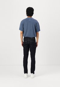 Blue short-sleeve t-shirt made of soft fabric, paired with dark denim jeans. The jeans feature a classic fit with back pockets. White sneakers.