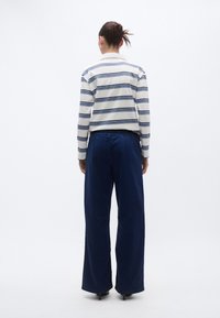 Camisa de manga larga a rayas en blanco y azul, combinada con pantalones anchos de color azul marino. La camisa cuenta con cuello y los pantalones tienen una sutil cintura elástica.