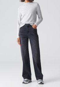 Luźne, czarne jeansy z wysokim stanem, pięcioma kieszeniami i zapięciem na guzik, połączone z jasnoszarym, teksturowanym topem z długim rękawem oraz sneakersami.