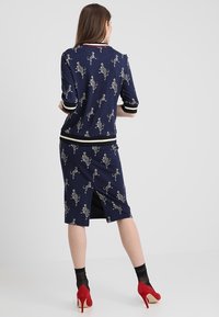 Marinblå klänning med katttryck, korta ärmar, randiga manschetter och nederkant, samt en rygget vent för ökad rörlighet. Röda högklackade skor.