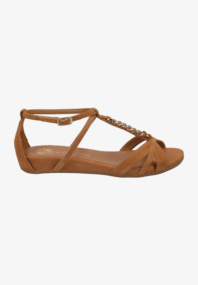 Sandales plates en suède marron avec bout ouvert, brides croisées, fermeture à boucle et détail de chaîne sur la partie supérieure.
