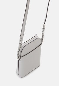 Borsa a tracolla in pelle grigia chiara con una texture liscia, chiusura con zip e dettaglio in catena argentata sulla tracolla. Forma rettangolare compatta.