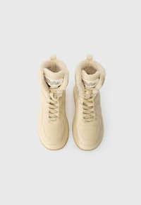 Κρεμίζινα ψηλά αθλητικά παπούτσια με υφασμάτινο γούνινο κολάρο, κορδόνια στο μπροστινό μέρος και πέλμα από καουτσούκ γουμά. Διαθέτει λεπτομέρειες με τρύπες.