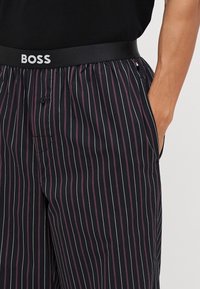 Mustra mustriga püksid pehme vöökohtaga, millel on "BOSS" logo, vertikaalsed jooned lillakas-hallides toonides, kaks külgtaskut ja lõdvestatud lõige.