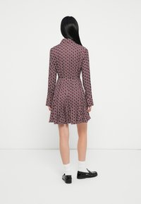 Sarkans un balts ziedu raksta kleita ar izplestu svārku, garām piedurknēm un jostu viduklī, izgatavota no gludas auduma. Melni apavi un baltas zeķes papildina kopskatu.