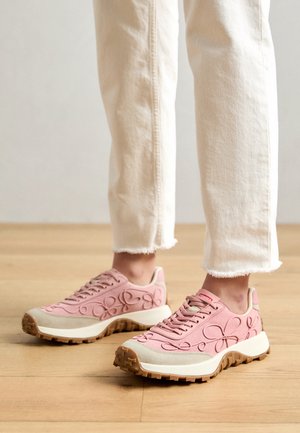 Rosa Turnschuhe mit geprägtem Blumendesign, kontrastierender hellbeiger Zwischensohle und strukturierter brauner Außensohle. Tragen mit cremefarbenen, ausgefransten Hosen.