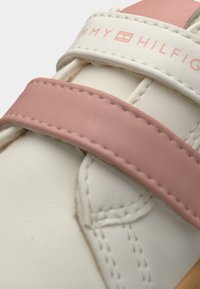 Λευκό και ροζ παπούτσι χωρίς κορδόνια με υφή που μοιάζει με δέρμα, με φαρδιές λωρίδες και ραφές. Λογότυπο της μάρκας στη λωρίδα.