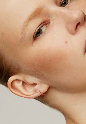 Pequeño pendiente de aro con piedras preciosas rosas, que presenta un delicado diseño retorcido. El modelo tiene el cabello corto y un sutil perfil de la oreja.