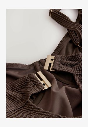 Costum de baie maro, fabricat dintr-un material texturat, cu accesorii din aur și detalii strânse pe bretele și margini. Căptușeală interioară netedă.