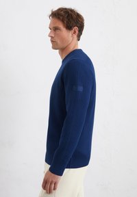 Marineblauwe geribbelde trui met een ronde hals en lange mouwen, met een gestructureerde afwerking en een klein merklabel op de linkermouw.