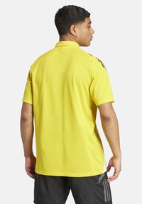 Geel kortemouwpoloshirt met een kraag, voorzien van zwarte accenten op de schouders en een gladde textuur. Achteraanzicht weergegeven.