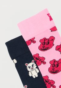 Ζευγάρι κάλτσες, η μία ροζ με κόκκινα καρτούν προσωπάκια σκύλων, η άλλη μπλε σκούρα με λευκά καρτούν προσωπάκια αρκούδων, και οι δύο διπλωμένες δίπλα-δίπλα.