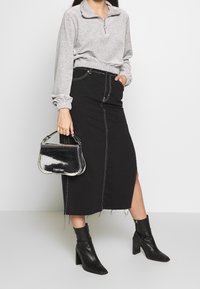 Grå zip-up fleece-top med elastisk midja, ihop med en svart denimkjol med vit sömnad och en sidoklyvning. Svarta klackiga ankelskor.