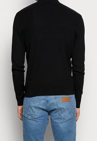 Svart stickad tröja med långa ärmar och rund halsringning, kombinerad med ljusblå jeans med ett lädermärke och zickzack-söm på bakfickorna.