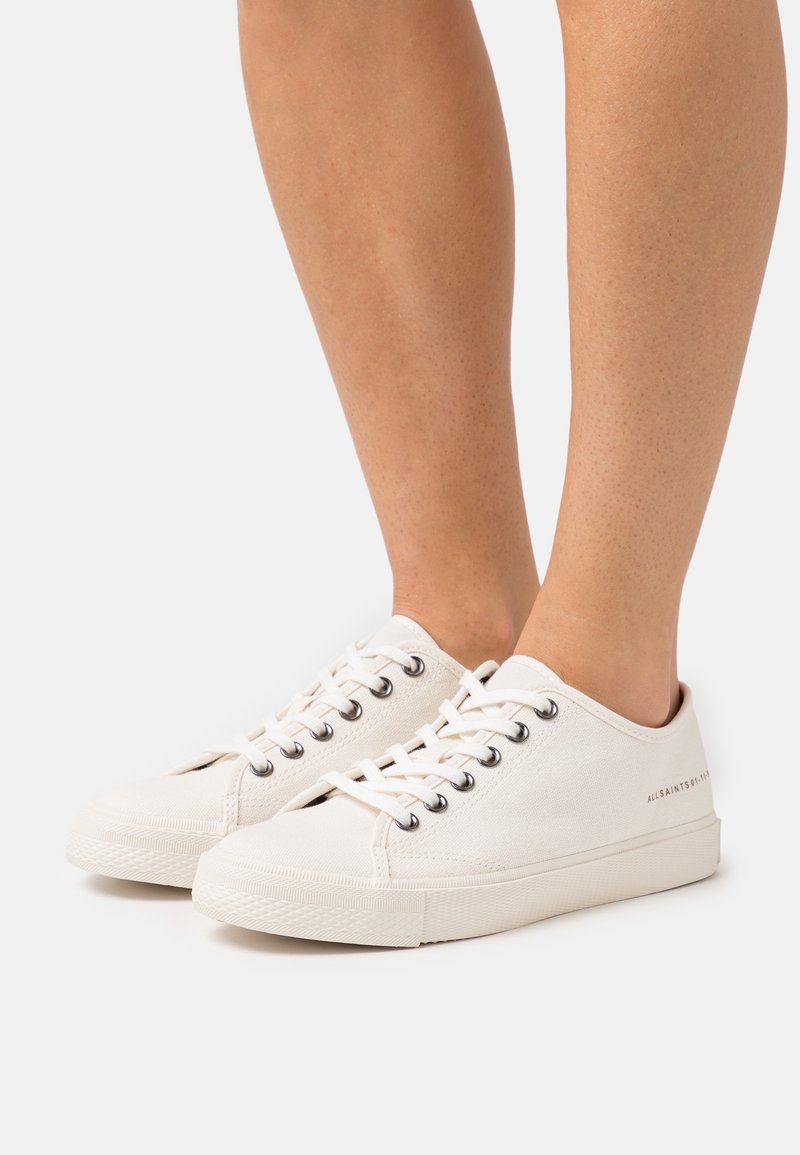 Vita canvas sneakers med rund tå, sex snörhål, texturerat material och subtil branding på sidan. Passar bra med avslappnad klädsel.