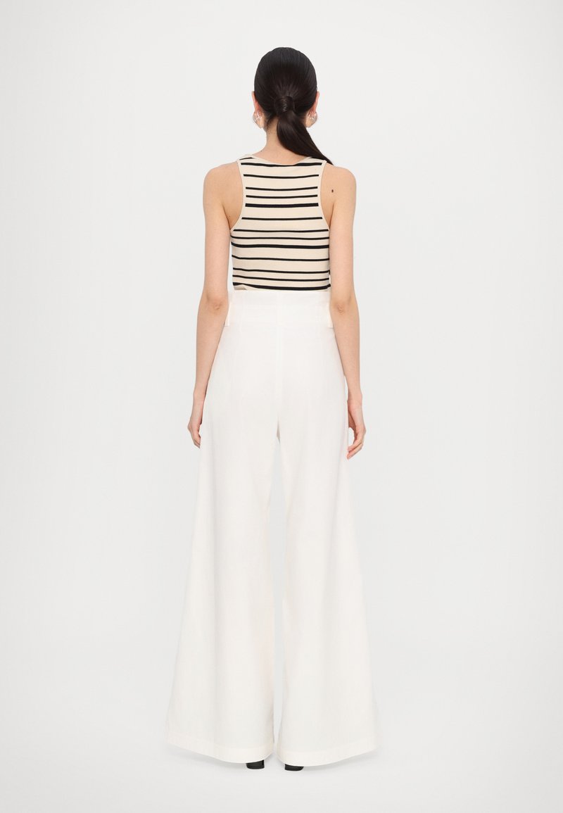 Striped beige tank top paired with high-waisted, wide-leg white trousers. Smooth fabric with a relaxed fit. Minimalist design and elegant silhouette.