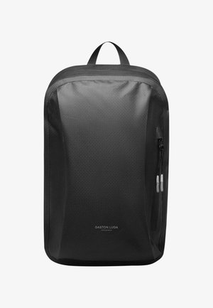 Svart ryggsekk med en teksturert overflate, glidelåslomme på siden og håndtak på toppen. Har et minimalistisk design med trykket merkevarelogo.