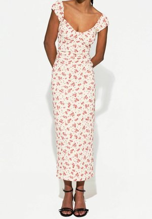 Robe midi florale avec un décolleté arrondi, des manches courtes et une silhouette ajustée dans un tissu crème avec de petites fleurs rouges. Sandales noires à lanières.