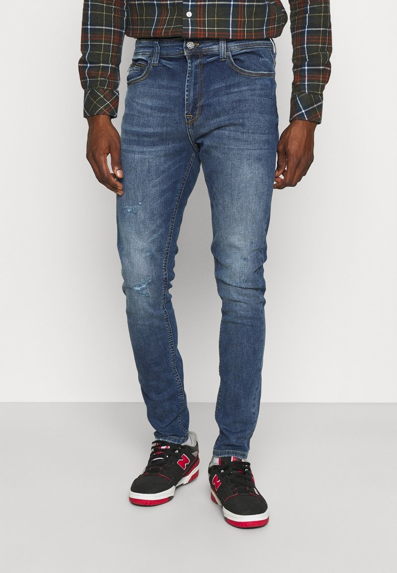 Modré skinny džiny vyrobené z denimu, s vybledlým umyvadlem, s opotřebovanými detaily a designem s pěti kapsami, v kombinaci s černými teniskami.