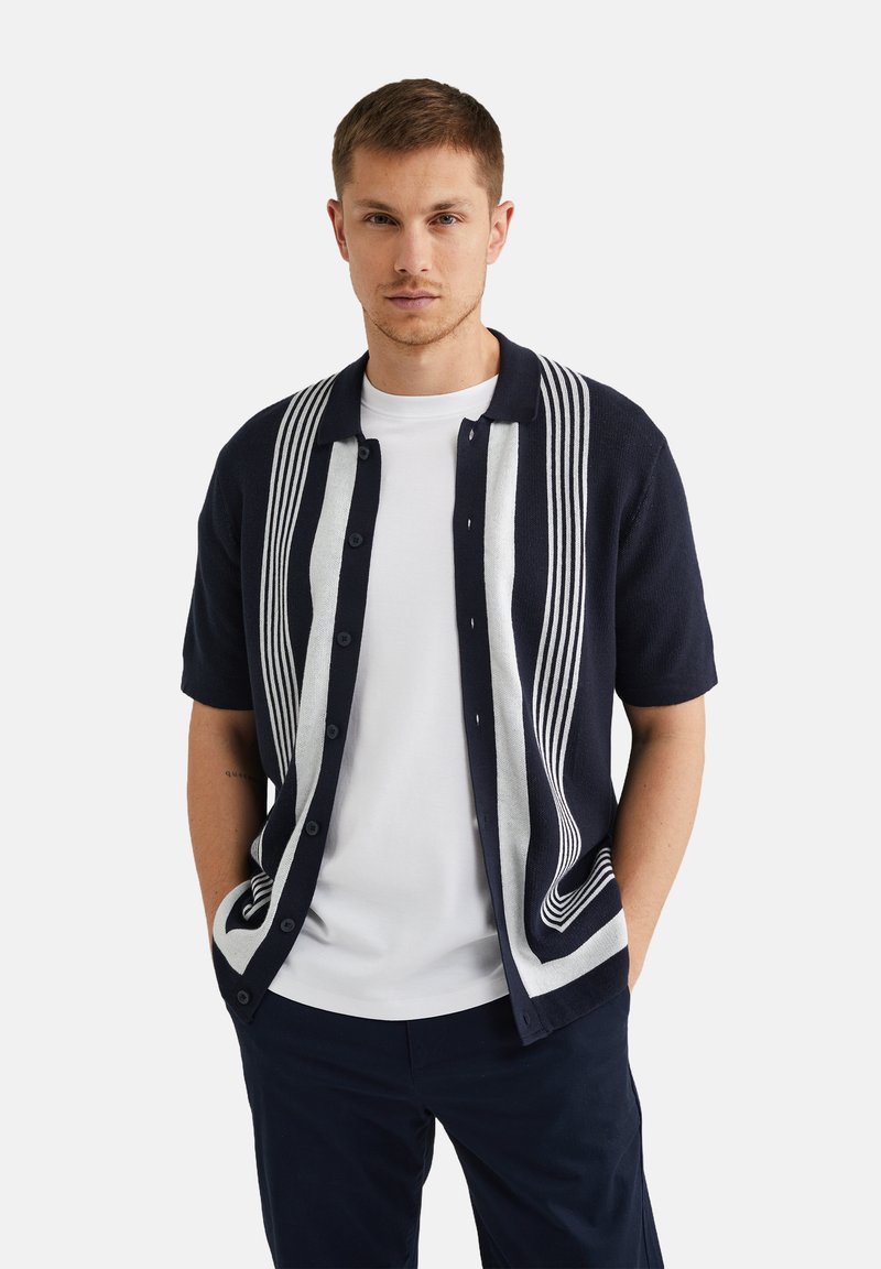 Navy cardigan with short sleeves, featuring white vertical stripes. Made of textured fabric with a buttoned front and a classic collar design.
