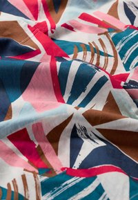 Buntes Gewebe zeigt abstrakte Muster in Blau, Pink und Rot mit überlappenden Formen und kräftigen weißen Akzenten. Glatte Baumwolltextur.