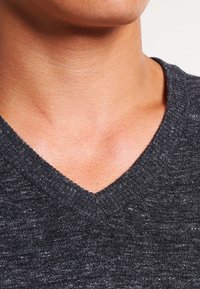 Ciemnoszara, dzianinowa sweter w serek o miękkiej fakturze, z prążkowanym kołnierzem i subtelnymi wariacjami we wzorze materiału.