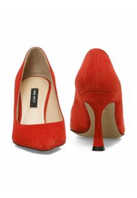 Zapatos de tacón alto de ante rojo con punta afilada y un tacón delgado, que cuentan con un forro interior suave y un sutil acento negro en la suela.