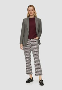 Blazer gris sur un pull côtelé bordeaux et un pantalon évasé à motifs rouge, vert et blanc. Chaussures plates noires avec une semelle épaisse.