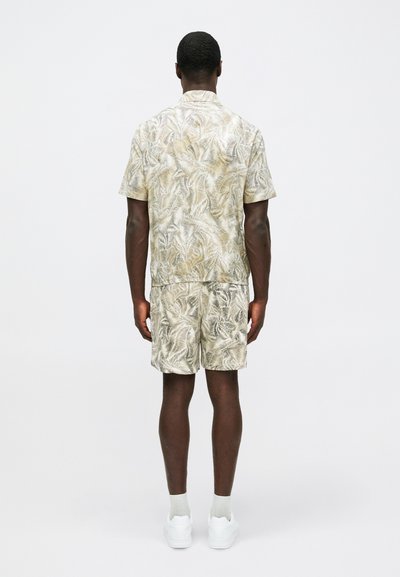 Ensemble chemise à manches courtes et short en beige clair avec un motif de feuilles de palmier. Fabriqué dans un tissu lisse, il présente une coupe décontractée et une taille élastique.