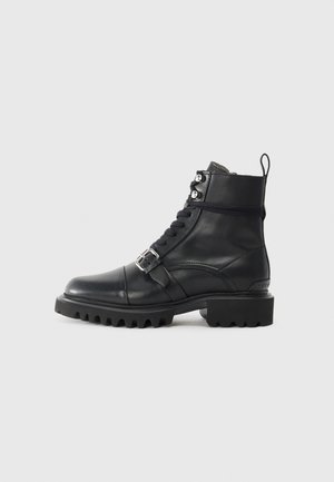 Stivaletto in pelle nera con punta rotonda, lace-up frontale, dettaglio con fibbia e suola spessa e robusta. Presenta accenti in metallo di tonalità argentata.