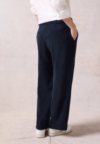 Navy wijde broek van zacht materiaal, met zijzakken en een eenvoudig ontwerp aan de achterkant. Gepoederd met witte schoenen.