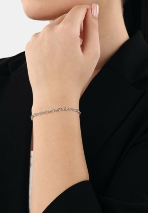 Bracciale in argento su un polso, con anelli circolari dalla finitura liscia. La mano poggia delicatamente su una giacca nera.