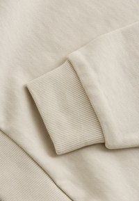 Tissu de sweat-shirt beige avec un bord-côte côtelé. La texture est douce et lisse, avec des détails de couture subtils. Design simple et minimaliste.