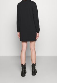 Black long-sleeve dress with a relaxed fit, featuring a round neckline. Worn with black ankle boots, showcasing a textured design.