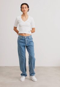 T-shirt blanc crop à manches courtes et col en V, associé à un jean large bleu clair. Porté avec des baskets blanches.
