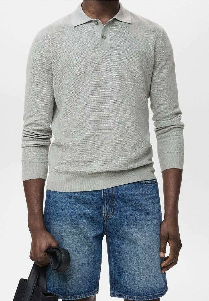 Homme portant un polo gris clair à manches longues et un short en jean bleu, tenant un sac noir dans une main sur fond blanc.