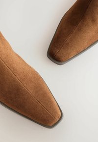 Rudos suede aulinukai iki kulkšnies su smailiais pirštais ir minimaliais juodais padeliais. Viršus pasižymi lygiu paviršiumi ir tvarkingomis siūlėmis.