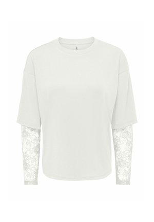 Chemise blanche à style superposé avec manches courtes sur des manches longues en dentelle transparente à motif floral.