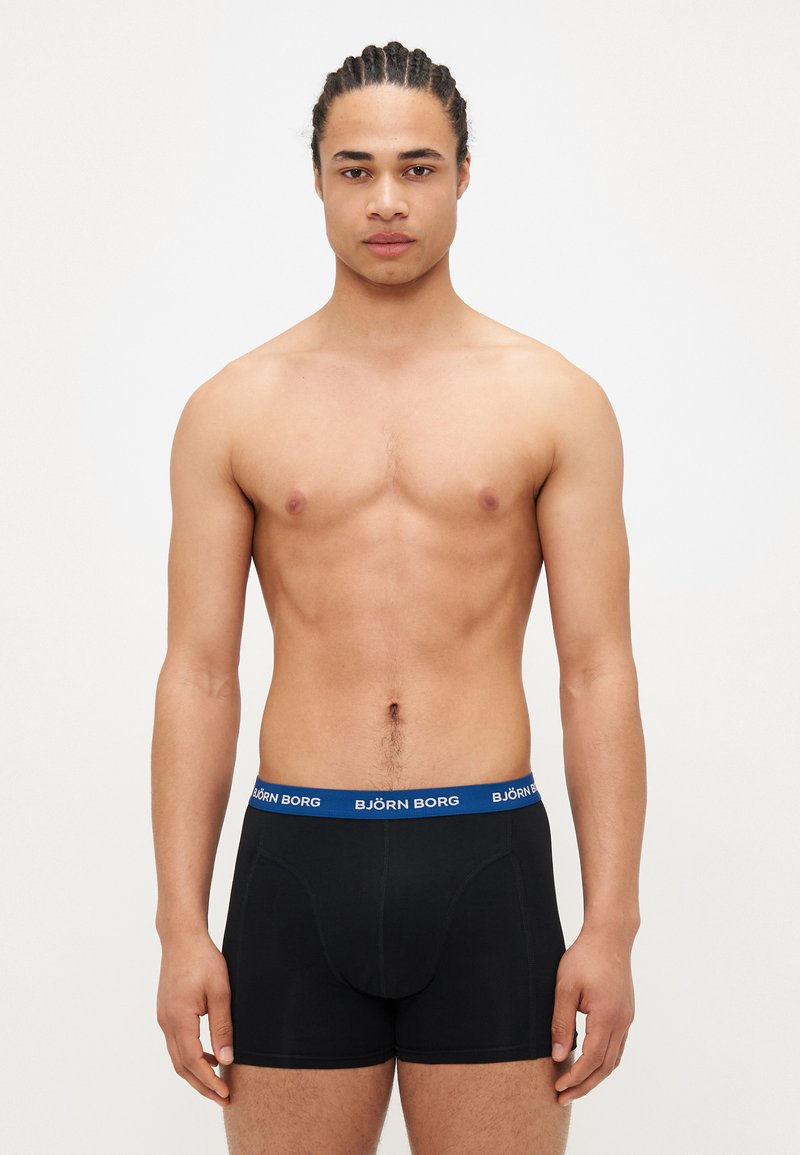 Boxer shorts noirs avec une ceinture élastique bleue arborant le logo « BJÖRN BORG ». Le tissu semble lisse et ajusté.