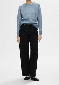 Vaaleansininen neulottu villapaita, jossa on ribbineulotut kalvosimet, yhdistetty korkeavyötäröisiin mustiin leveälahkeisiin farkkuihin ja yksinkertaisiin mustiin tasapohjaisiin kenkiin.