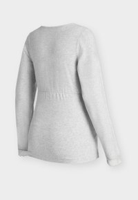 Světle šedý top s dlouhým rukávem, kulatým výstřihem a nařaseným pasem, s krajkovým lemem na rukávech pro zvýraznění detailů a textury.