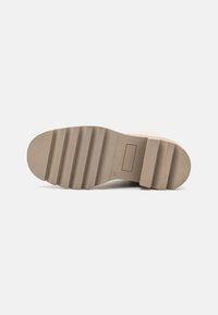 Semelle de chaussure en caoutchouc beige avec plusieurs rainures et crêtes, design plat, détail rectangulaire et texture lisse.